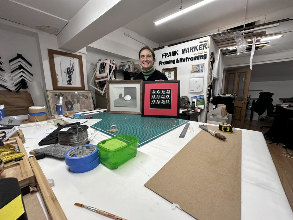 A smiling student holding two pieces she framed at Frank Marker Framers, Govan, Glasgow